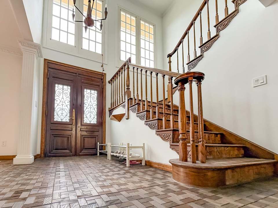 Entry hall with carved double doors, tall windows and a curving carved-wood staircase
