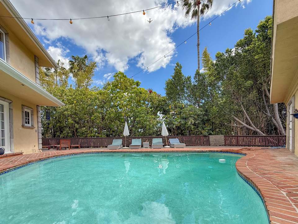 The oval saltwater pool on its terracotta-brick deck, with loungers under white fringe umbrellas and tall trees behind