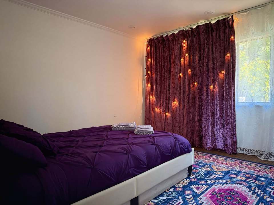 Queen bedroom with purple bedding and heavy blackout drapes