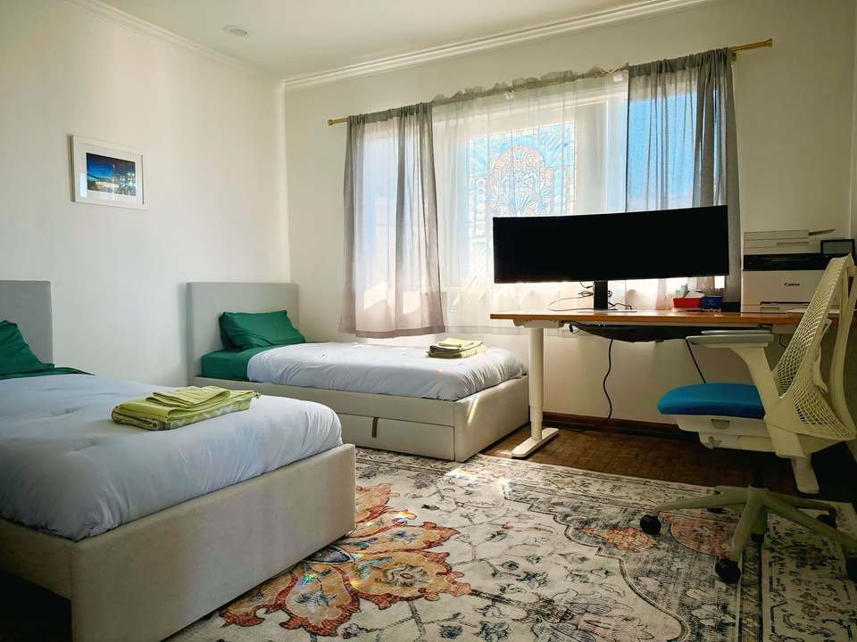 Twin bedroom with two single beds and a sit/stand desk with a 49-inch ultra-wide monitor