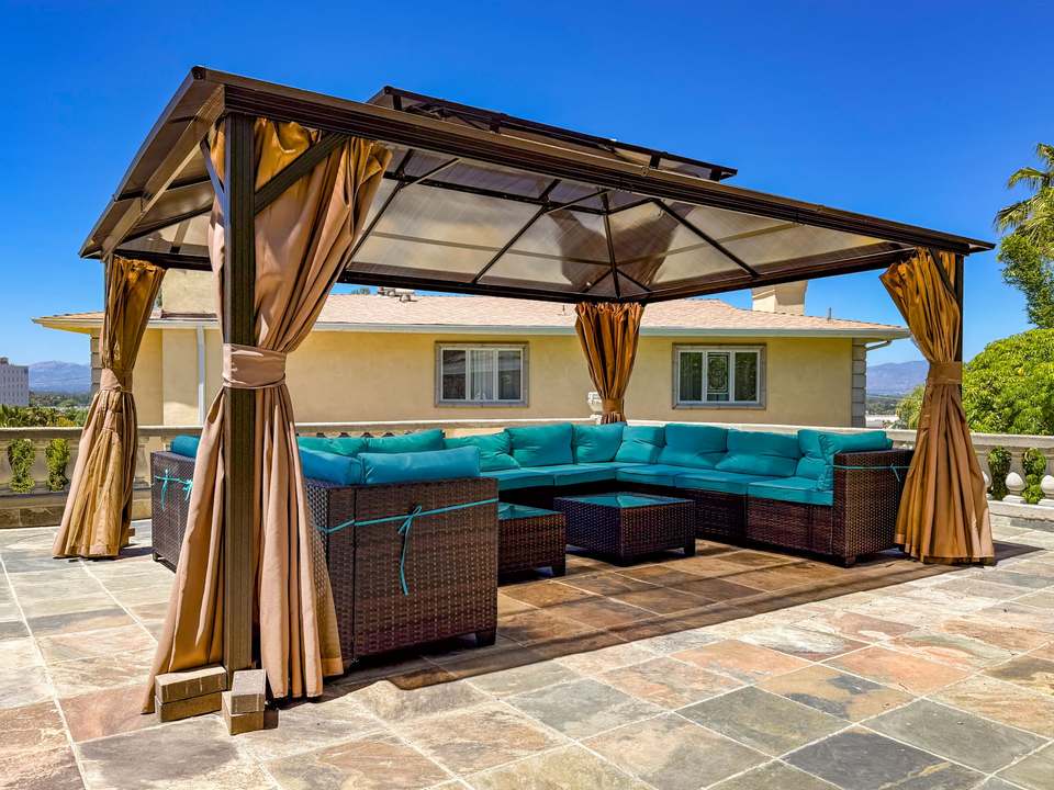Rooftop gazebo on a slate-tile patio with curtains tied back and mountains beyond