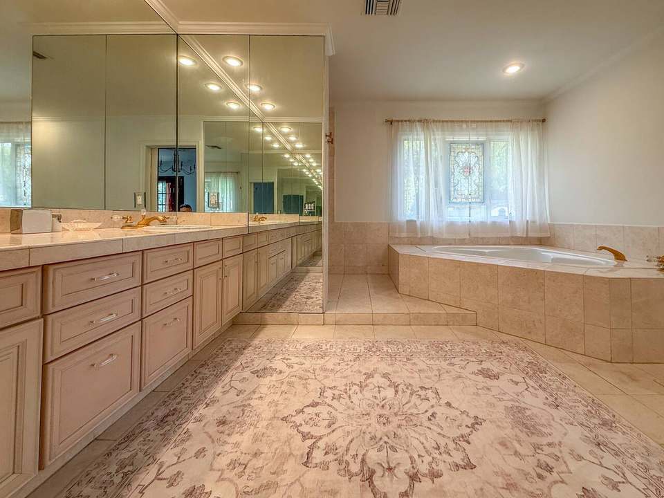 Primary bath with a long double vanity, mirrored wall and corner soaking tub