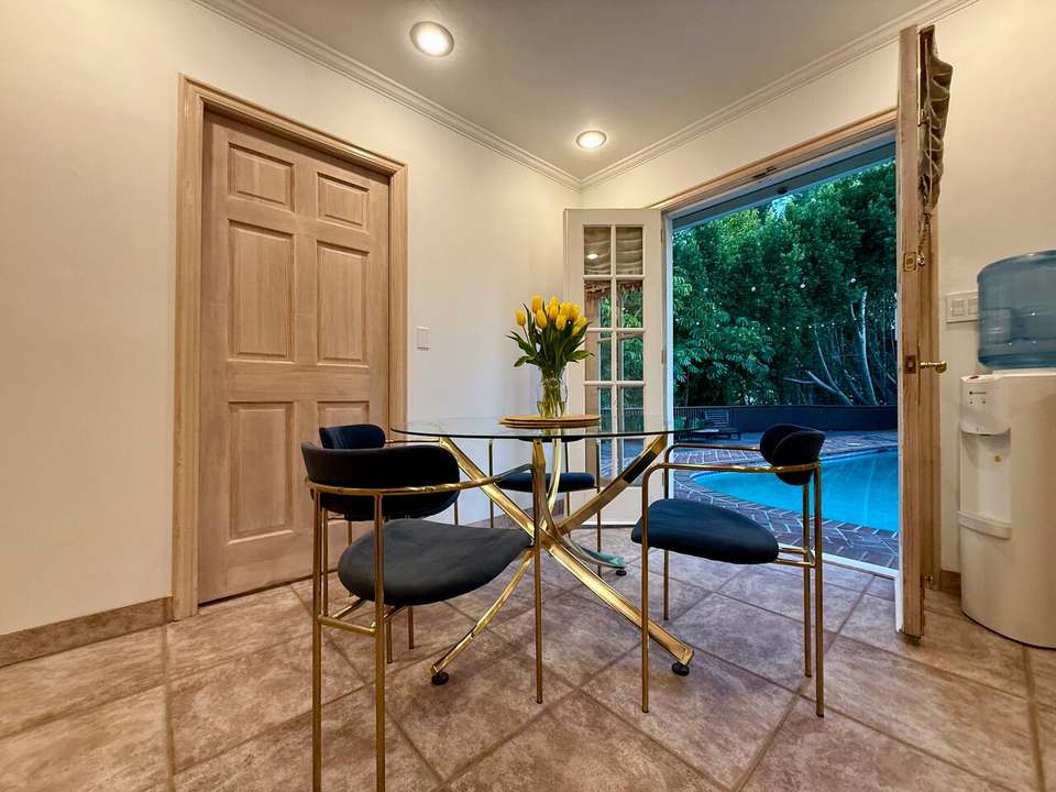 Breakfast nook with a glass table and velvet chairs beside French doors to the pool