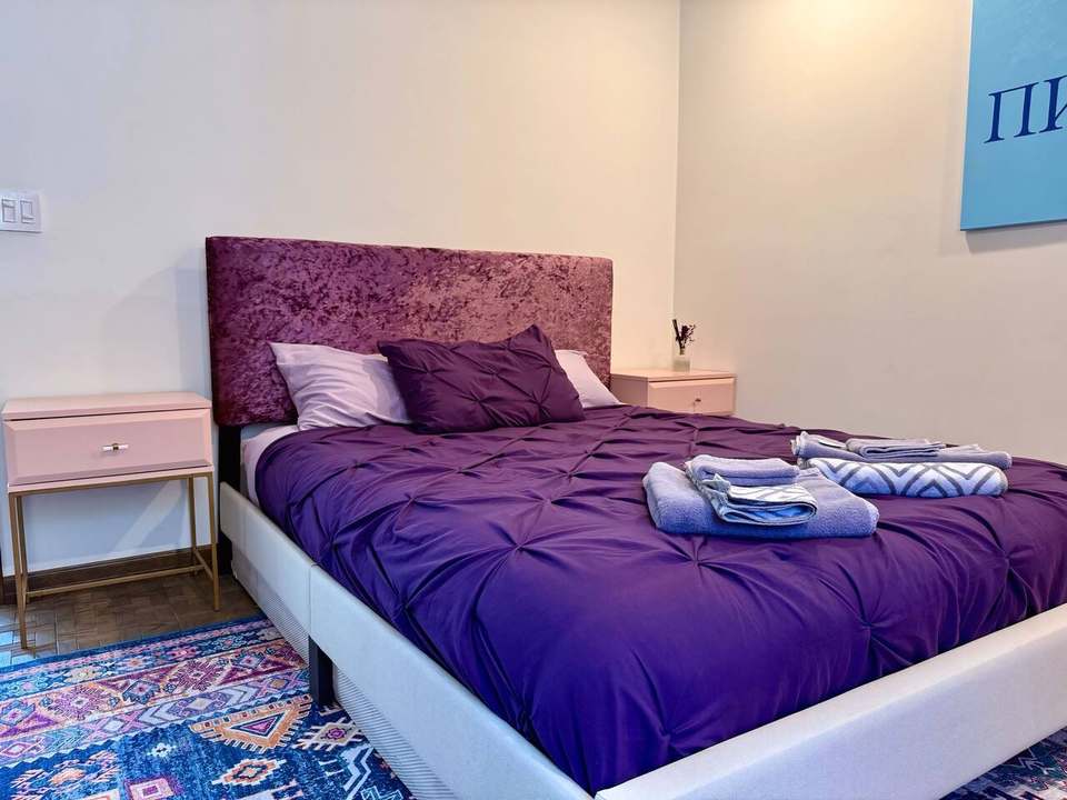 Queen bedroom with a purple velvet headboard and pink nightstands