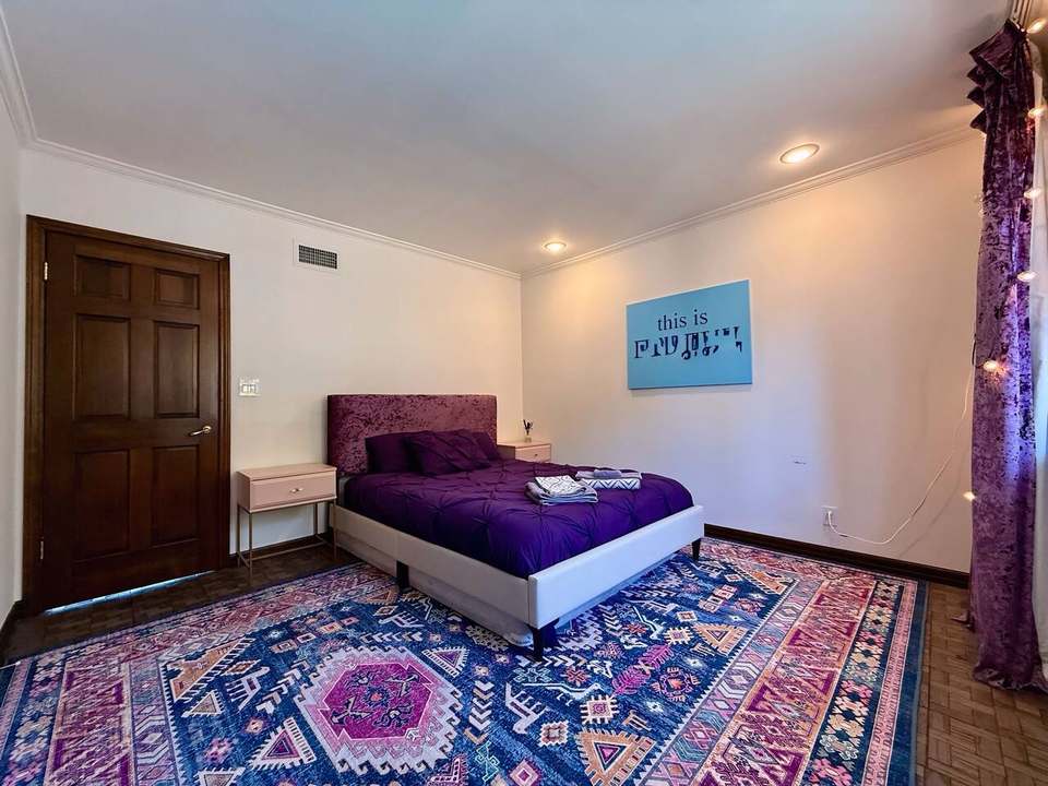 Queen bedroom with purple bedding and a patterned boho rug