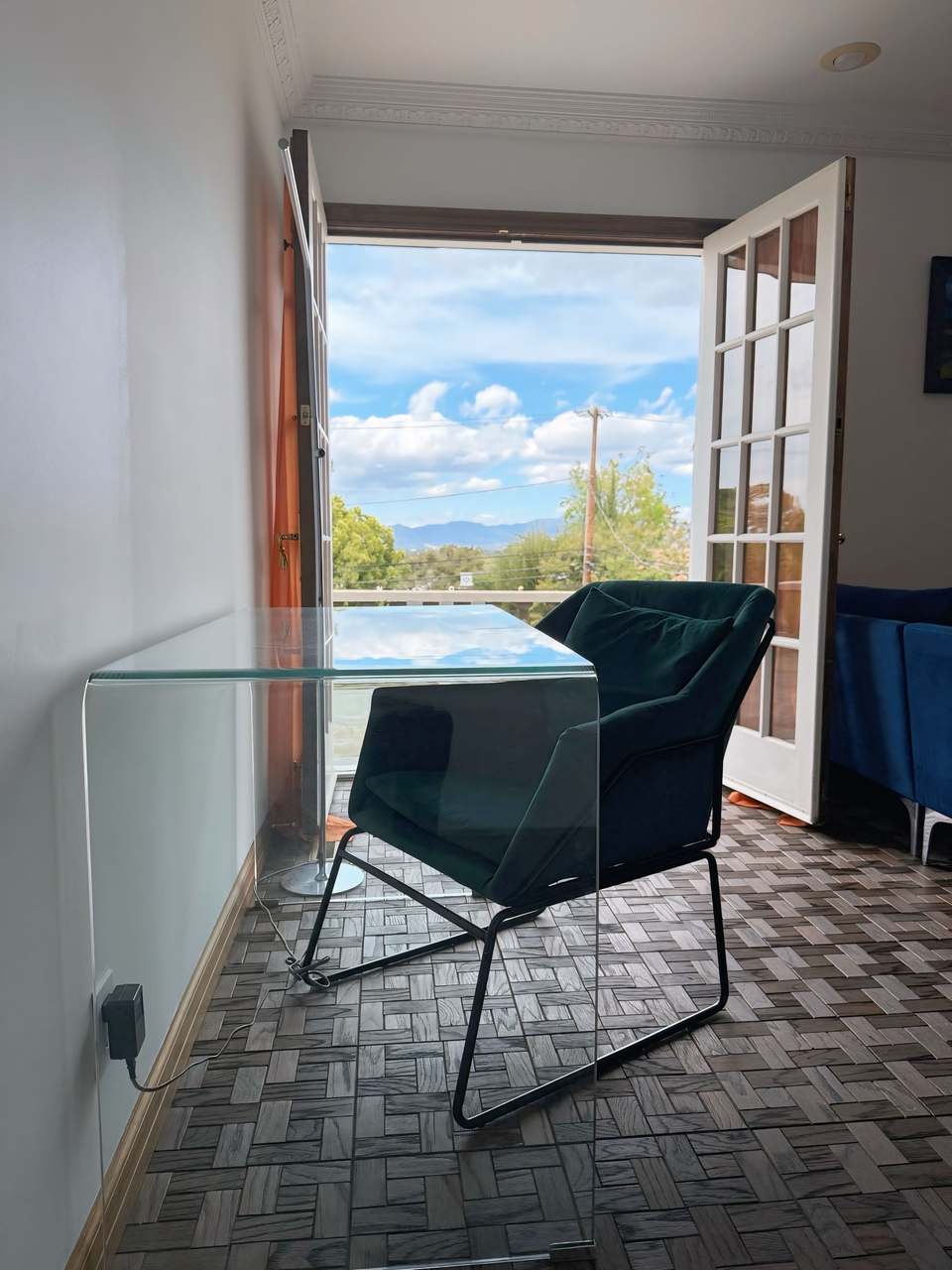 Glass desk and chair by open French doors with a view of trees and sky